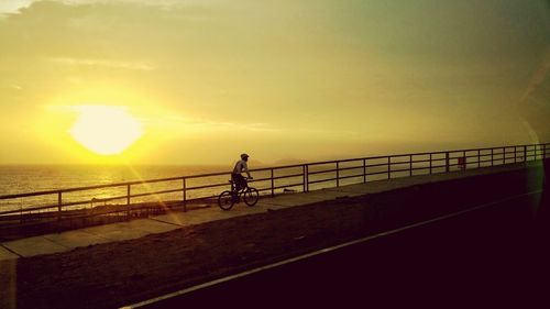 Silhouette man riding bicycle on sea against sky during sunset