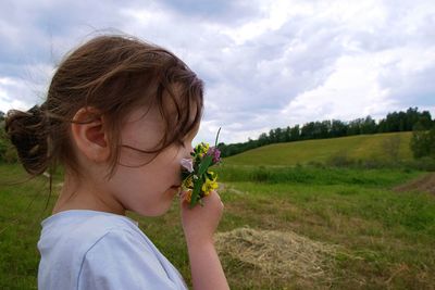 Close-up of girl with flowers on field against sky