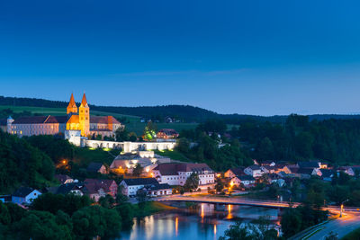 Illuminated buildings by river against blue sky