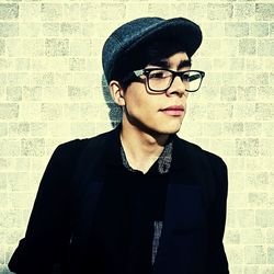 Portrait of young man wearing eyeglasses standing against wall