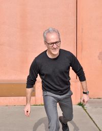 Happy mature man walking against brown wall