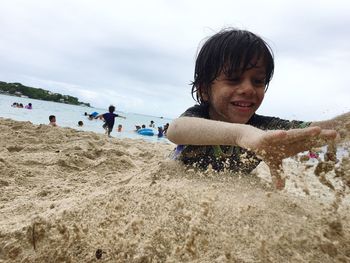 Boy buried in sand while playing at beach against sky