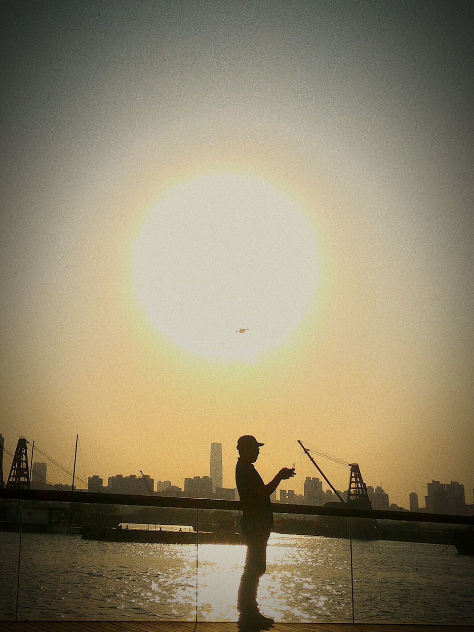 SILHOUETTE MAN FISHING AT RIVERBANK AGAINST CLEAR SKY