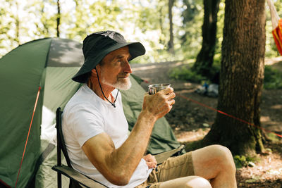 Young man drinking water while sitting in forest