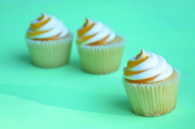 3 orange and white swirl top mango flavor cupcakes on green surface