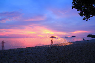 Woman spinning wire wool on beach against sky during sunset