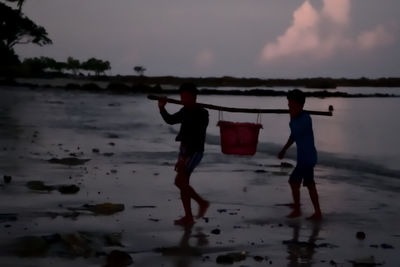 Men standing on beach against sky during sunset