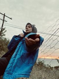 Portrait of young woman standing against sky