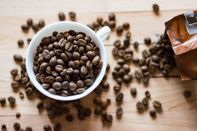 Directly above view of roasted coffee beans scattered by cup on table