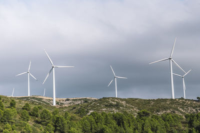 Windmills in field against cloudy sky