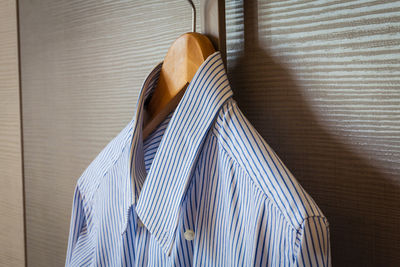 Close-up of striped shirt hanging coathanger by wooden wall