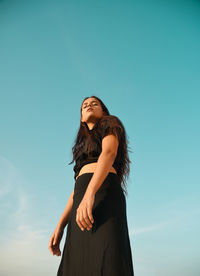 Low angle view of woman looking away against blue sky