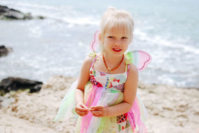 Portrait of little girl in butterfly costume standing at beach