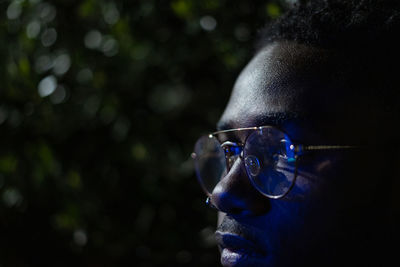 Close-up of man wearing eyeglasses in illuminated city at night