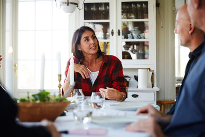 Mature woman talking with male friends while sitting at dining table