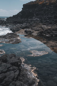 Rocks on shore by sea against sky