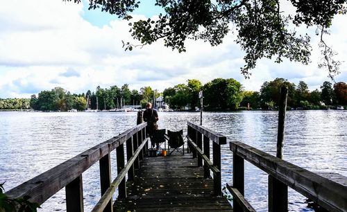 People sitting on jetty by river against sky