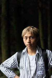 Portrait of serious young man standing by trees