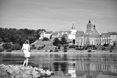 Rear view of woman standing by river against sky