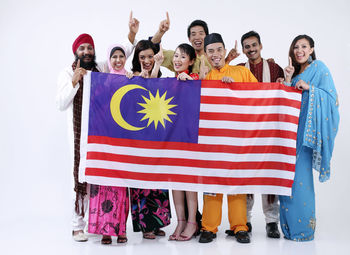 Portrait of happy people wearing traditional clothing holding malaysian flag against white background
