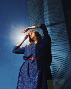 Low angle view of woman standing against wall on sunny day