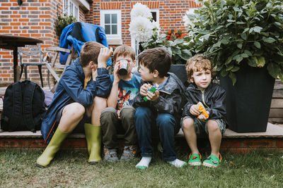 Full length of friends sitting at backyard against house