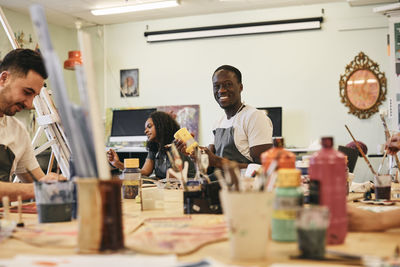 Portrait of happy young man holding paint container in art class