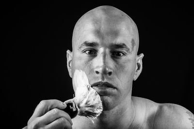 Close-up portrait of shirtless bald man applying shaving cream against black background