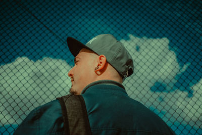 Portrait of man wearing hat seen through chainlink fence