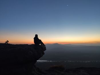 Silhouette man standing on rock against sky during sunset