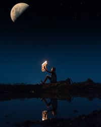 Man standing on illuminated lamp against blue sky at night