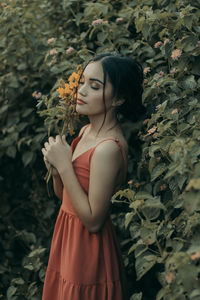 Portrait of young woman standing against plants