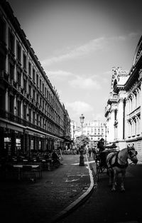 People walking on street amidst buildings in city against sky