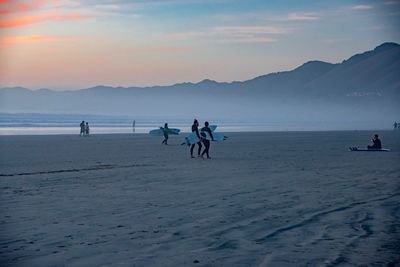 People at beach against sky during sunset