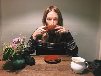 Portrait of young woman drinking coffee at table in cafe