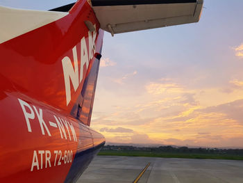 View of airplane at airport runway against sky during sunset