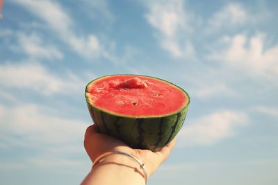 Close-up of hand holding strawberry against sky