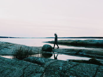 Mid distant view of woman walking at beach against sky during dusk