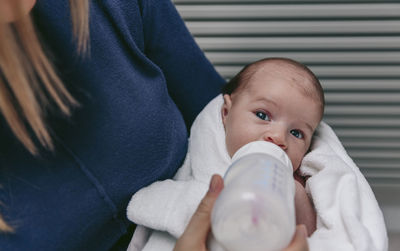 Midsection of mother feeding son with milk bottle