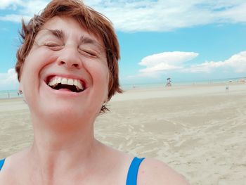 Close-up of woman laughing while standing at beach against sky