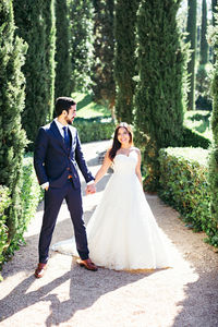 Happy newlywed couple holding hands while standing on footpath at park