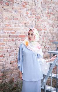 Portrait of young woman standing against brick wall