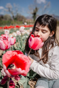 Close up view of girl in white dress smelling big flower sitting in tulip field
