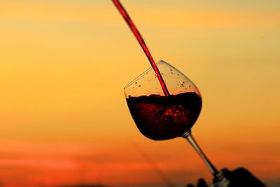 Close-up of wineglass against sky during sunset