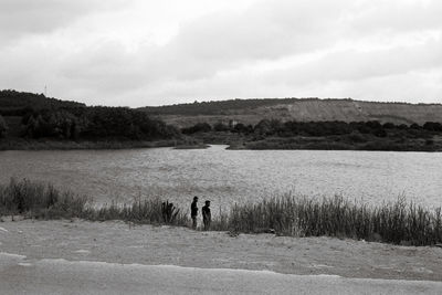 Men standing by lake against sky