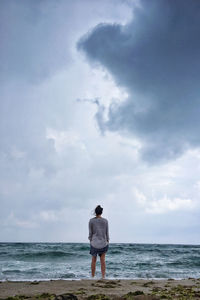 Rear view of man standing on beach against sky