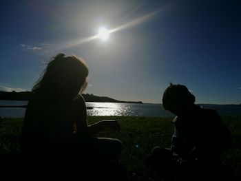 Rear view of silhouette girl sitting by sea against clear sky