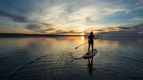 Silhouette woman paddleboarding in lake against sky