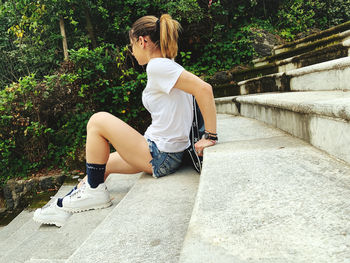 Full length of young woman sitting on retaining wall