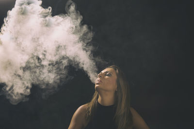 Close-up of young woman smoking against black background